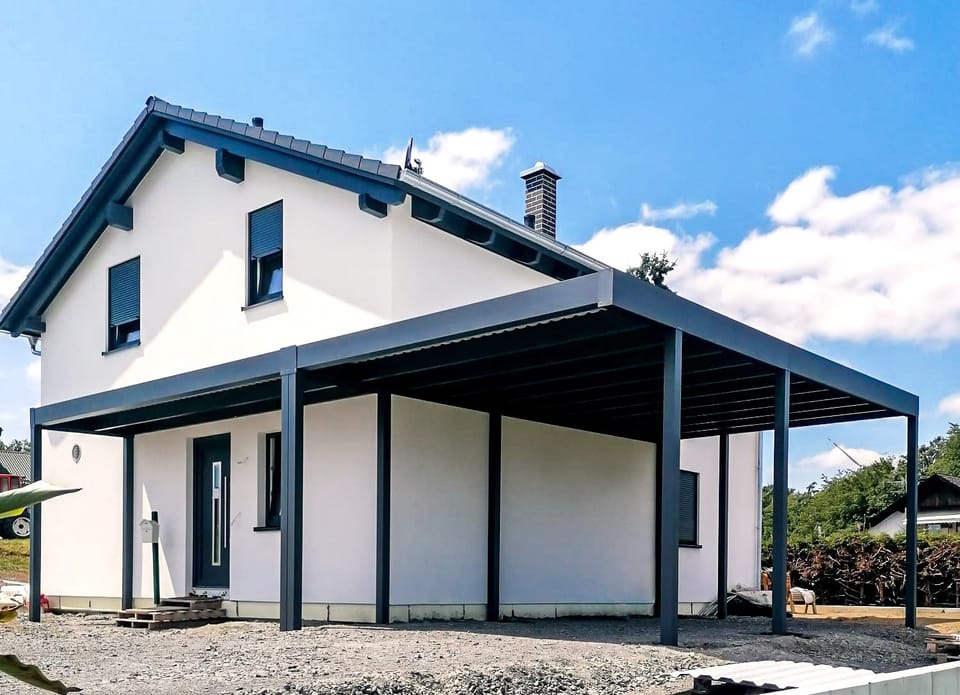 Großer anthrazitfarbener Aluminium-Carport an einem weißen Einfamilienhaus