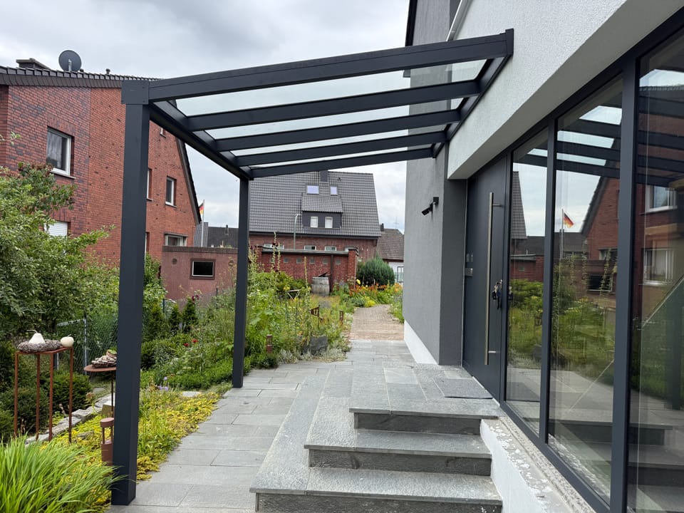 Neu montiertes Terrassendach an einem Haus mit Treppe und Garten